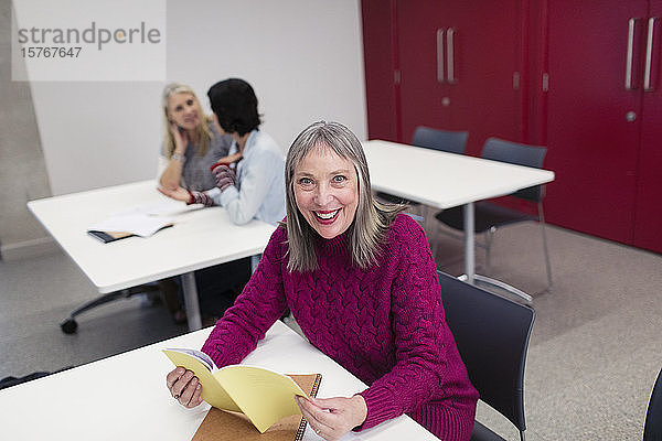 Porträt einer lächelnden  selbstbewussten Studentin einer Volkshochschule  die im Klassenzimmer liest