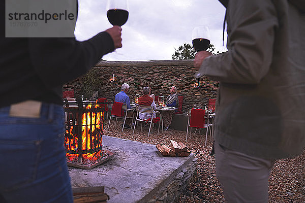 Ehepaar und ältere Freunde speisen und trinken Wein auf einer Terrasse mit Feuerstelle