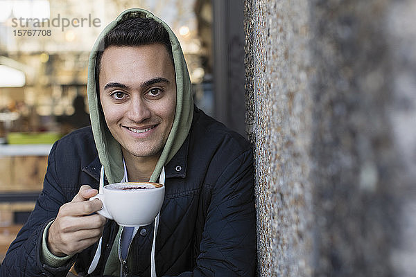 Porträt eines lächelnden  selbstbewussten jungen Mannes  der in einem Straßencafé Kaffee trinkt