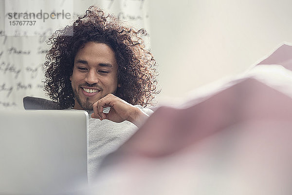 Lächelnder junger Mann mit Laptop auf dem Sofa