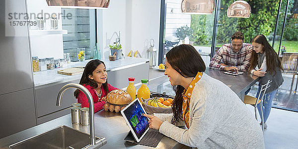 Familie im Gespräch  mit digitalen Tablets in der Küche