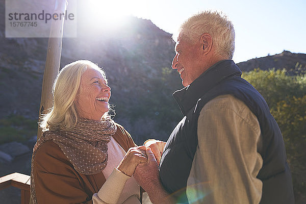 Glückliches älteres Paar hält sich auf einem sonnigen Balkon an den Händen