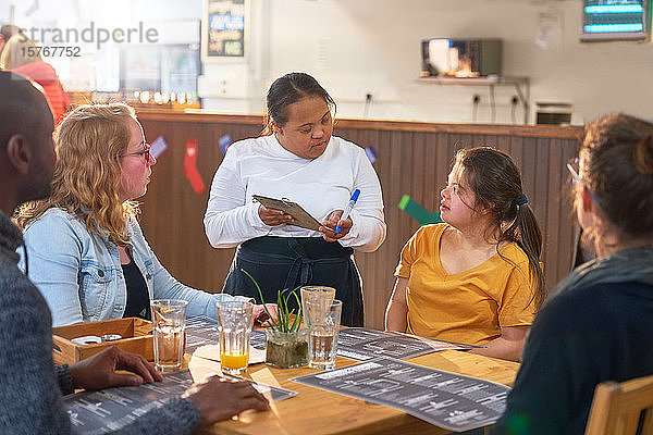 Junge Kellnerin mit Down-Syndrom nimmt in einem Café eine Bestellung auf