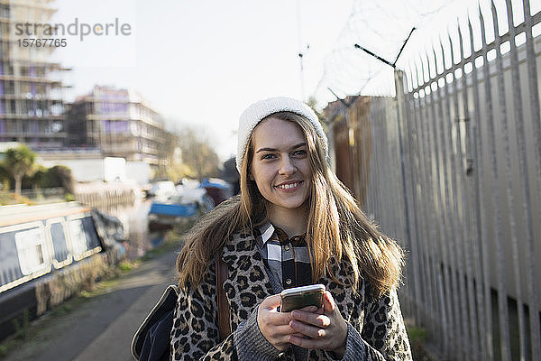 Porträt lächelnde junge Frau mit Smartphone auf städtischem Bürgersteig