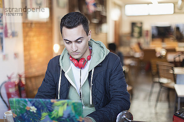 Fokussierter junger männlicher Student  der am Laptop in einem Caféfenster lernt