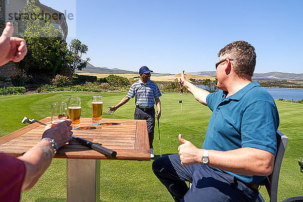 Männliche Golfer trinken Bier und feuern ihre Freunde auf dem Übungsgrün an.