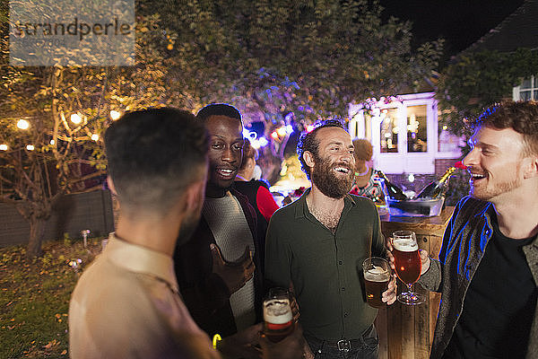 Männliche Freunde unterhalten sich und trinken auf einer Gartenparty