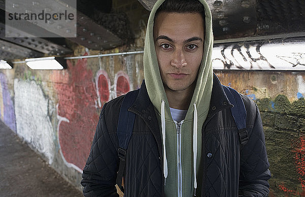 Porträt eines ernsten  taffen jungen Mannes mit Kapuzenpulli in einem städtischen Tunnel