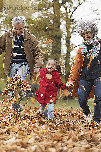 Verspielte Großeltern und Enkelin treten Herbstblätter im Park