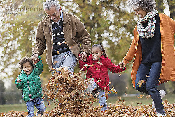Verspielte Großeltern und Enkelkinder beim Kicken von Herbstblättern im Park