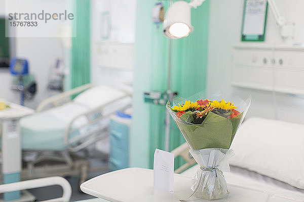 Blumenstrauß und Grußkarte auf einem Tablett in einem leeren Krankenhauszimmer