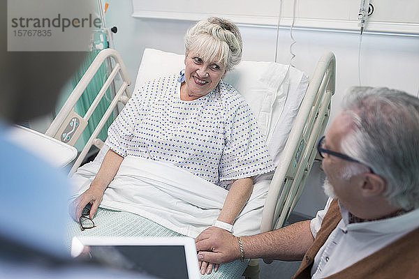 Zärtlicher älterer Mann im Gespräch mit seiner im Krankenhausbett liegenden Frau