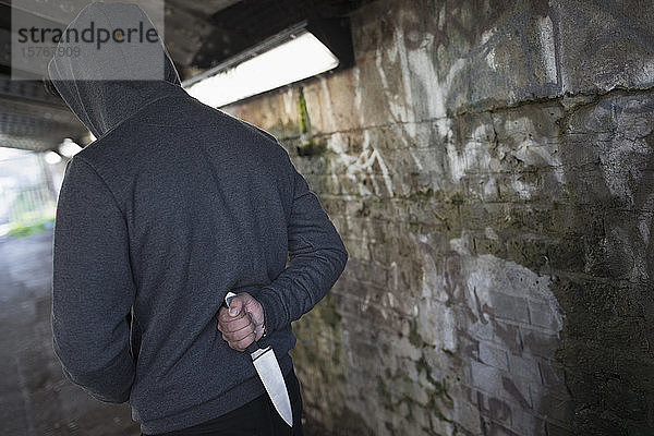 Gefährlicher Mann mit Messer im Rücken in städtischem Tunnel