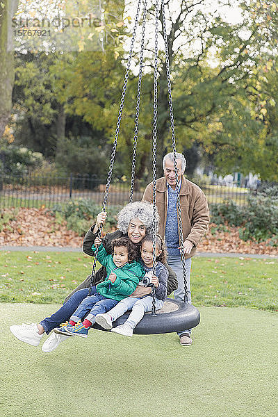 Großeltern und Enkelkinder spielen auf einer Reifenschaukel im Park