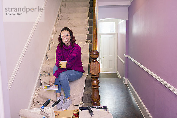 Porträt einer selbstbewussten Frau  die eine Treppe renoviert und sich ein Farbmuster ansieht