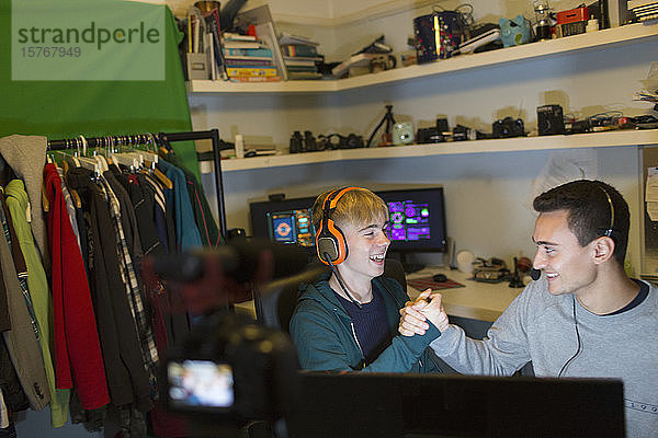 Glückliche Teenager mit Kopfhörern spielen ein Videospiel am Computer im Schlafzimmer