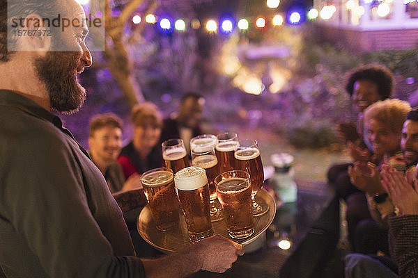 Mann serviert Freunden bei einer Gartenparty ein Tablett mit Bieren