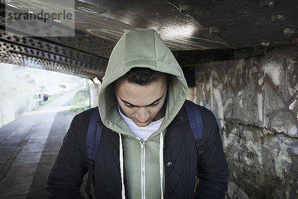 Junger Mann im Kapuzenpulli geht unter einer städtischen Brücke