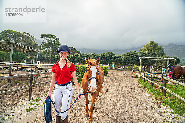 Porträt selbstbewusstes Teenager-Mädchen  das ein Pferd über eine ländliche Koppel führt