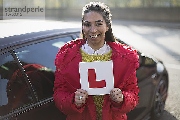 Porträt einer selbstbewussten  glücklichen jungen Frau mit Führerschein im Auto