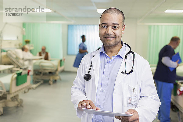 Porträt eines selbstbewussten männlichen Arztes bei der Visite  der ein digitales Tablet in einer Krankenhausabteilung benutzt