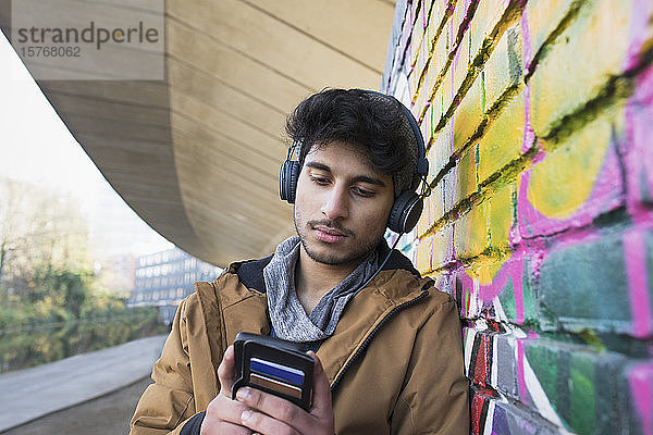 Junger Mann mit Kopfhörern  der auf einem städtischen Bürgersteig Musik hört