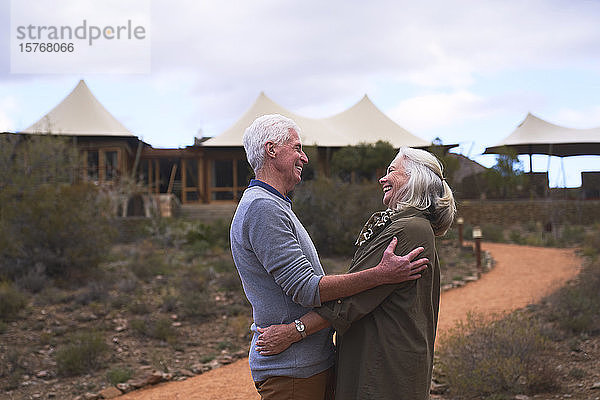 Zärtliches älteres Paar  das sich vor einem Safari-Lodge-Hotel umarmt