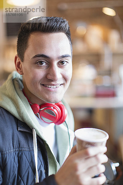 Porträt eines lächelnden  selbstbewussten jungen Mannes  der in einem Café Kaffee trinkt