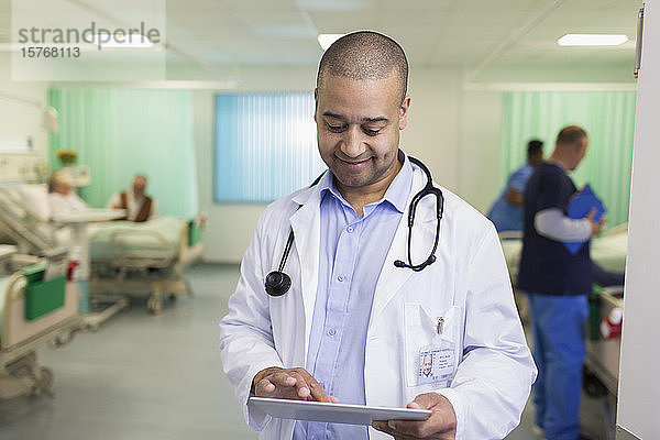 Lächelnder männlicher Arzt mit digitalem Tablet bei der Visite in einer Krankenstation