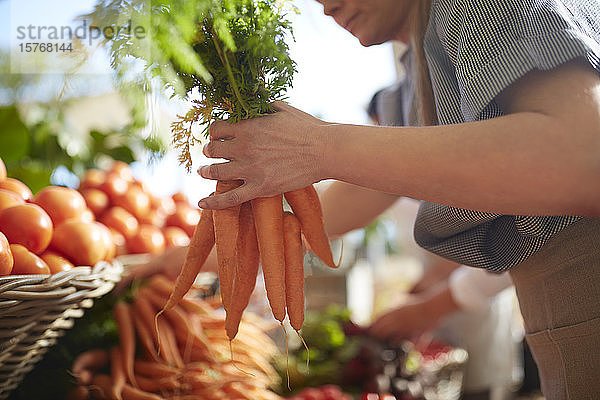 Frau hält ein Bündel Karotten auf dem Bauernmarkt