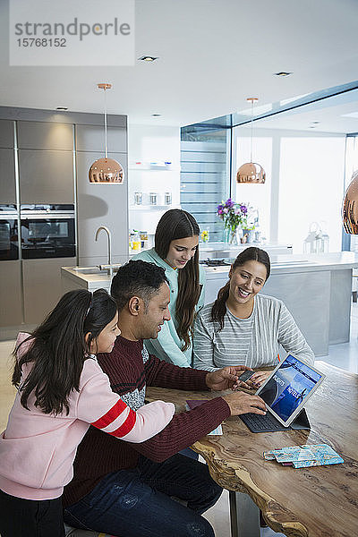 Glückliche Familie bei der Urlaubsplanung am digitalen Tablet am Esstisch