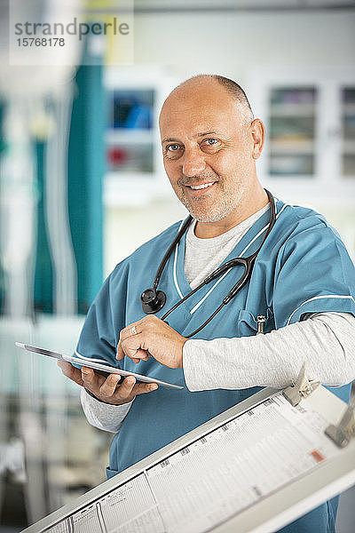 Porträt eines lächelnden  selbstbewussten männlichen Arztes  der ein digitales Tablet im Krankenhaus benutzt