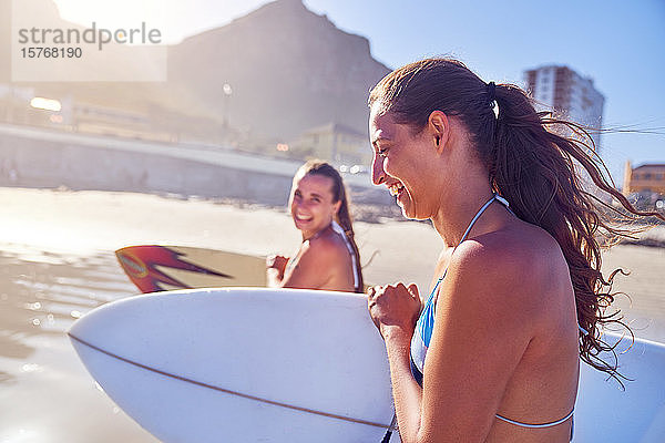 Glückliche junge Freundinnen mit Surfbrettern am sonnigen Strand