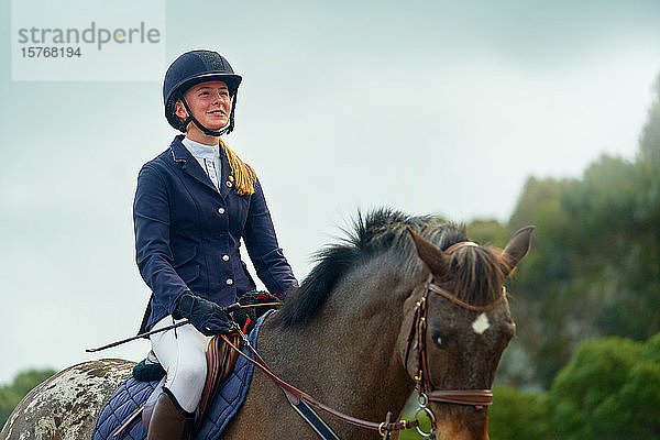 Selbstbewusst lächelndes Teenager-Mädchen reitet auf einem Pferd