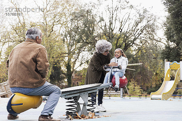Großeltern spielen mit Enkelin auf dem Spielplatz auf der Wippe