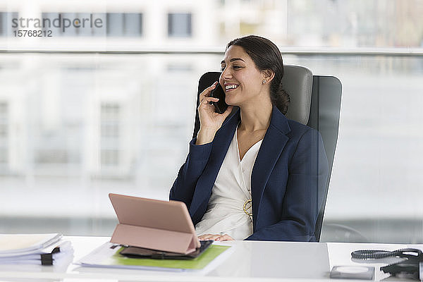 Lächelnde Geschäftsfrau  die im Büro mit einem Smartphone telefoniert