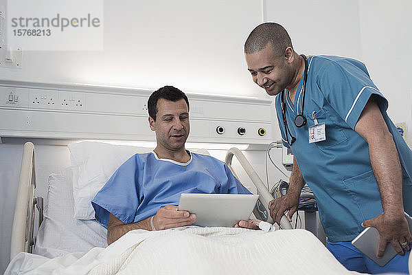 Männlicher Patient mit digitalem Tablet im Gespräch mit einer Krankenschwester im Krankenhauszimmer