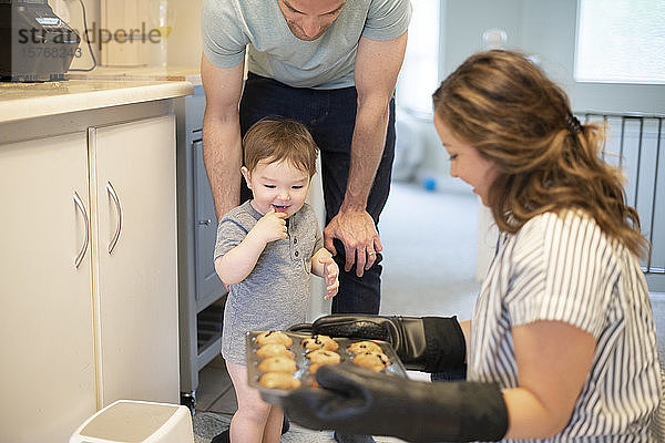 Neugieriges Kleinkind Mädchen beobachtet Mutter backen Muffins in der Küche