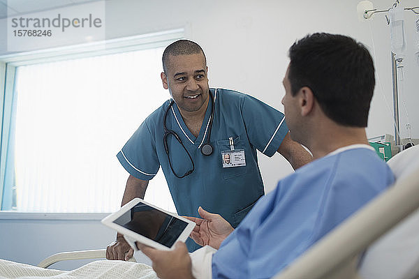 Krankenpfleger im Gespräch mit einem Patienten  der ein digitales Tablet im Krankenhausbett benutzt