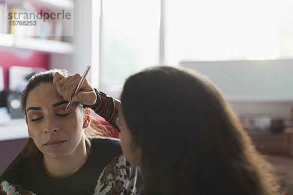 Teenager-Mädchen trägt Lidschatten-Make-up auf das Auge einer Freundin auf