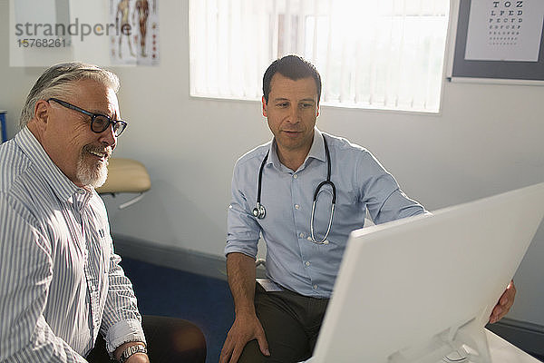 Männlicher Arzt trifft sich mit einem älteren Patienten am Computer in einer Arztpraxis