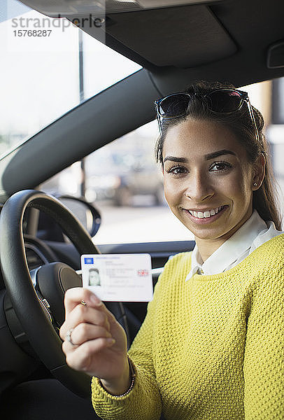 Porträt einer glücklichen jungen Frau mit neuem Führerschein im Auto