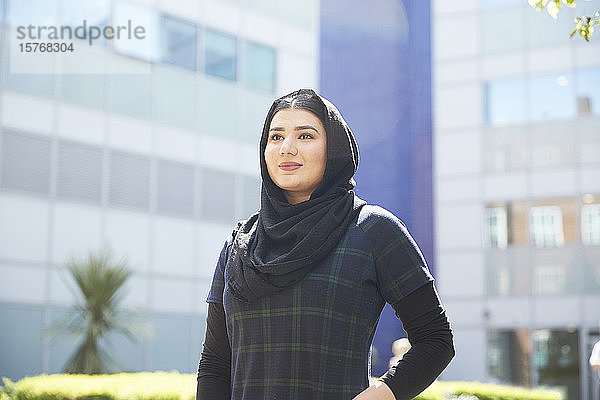 Porträt selbstbewusste junge Frau mit Hidschab vor einem sonnigen Gebäude