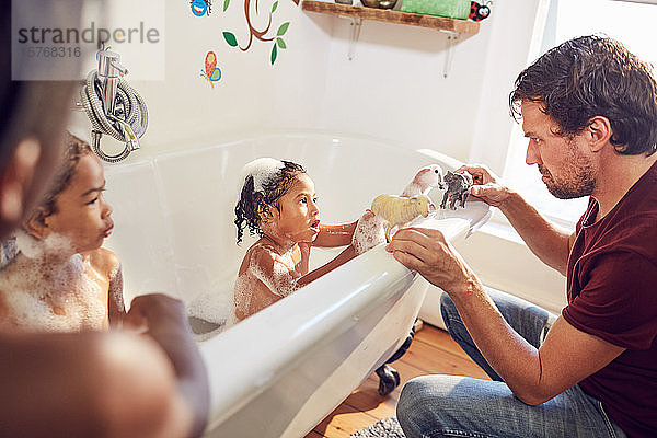 Vater und Tochter spielen in der Badewanne mit Spielzeugtieren