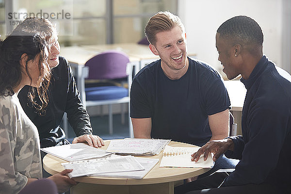 Glückliche junge Studenten  die sich unterhalten und in der Bibliothek lernen