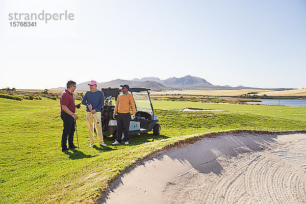 Männliche Golffreunde unterhalten sich im Sandloch auf einem sonnigen Golfplatz