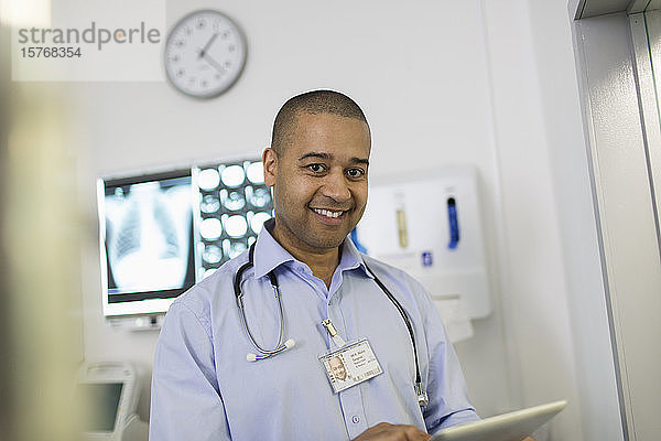 Porträt eines selbstbewussten  lächelnden männlichen Arztes  der ein digitales Tablet im Krankenhaus benutzt