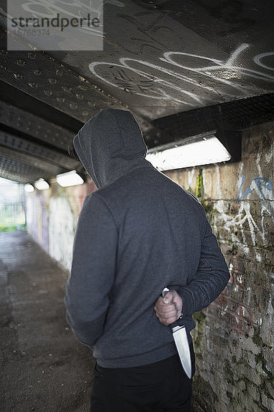 Gefährlicher junger Mann hält Messerwaffe hinter dem Rücken in städtischem Tunnel
