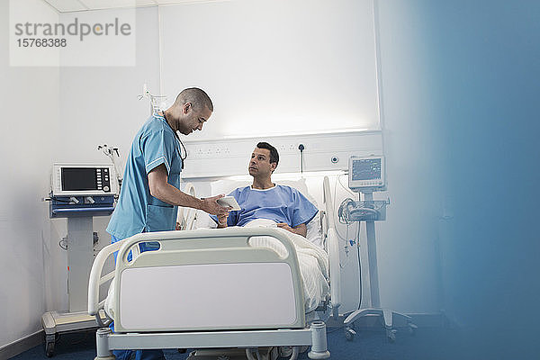Männlicher Arzt mit digitalem Tablet bei der Visite  im Gespräch mit einem Patienten im Krankenhauszimmer