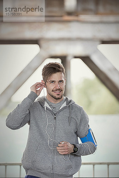 Porträt selbstbewusster junger männlicher Läufer mit Kopfhörern und mp3-Player-Armband